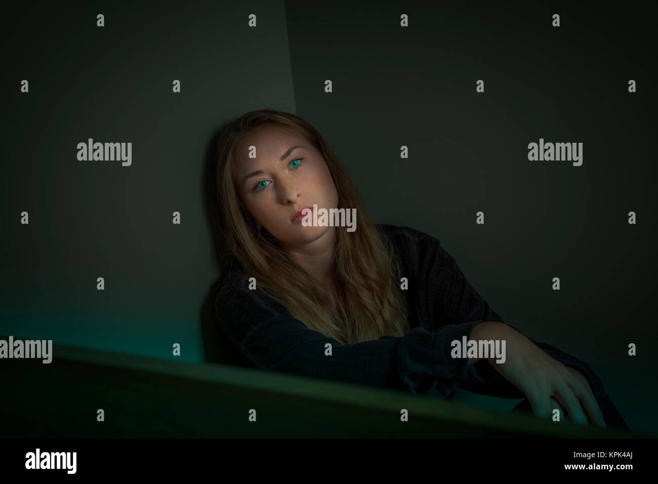 Junge Frau in einer Ecke sitzend mit intensiven grünen Augen in die Kamera schaut Stockfoto