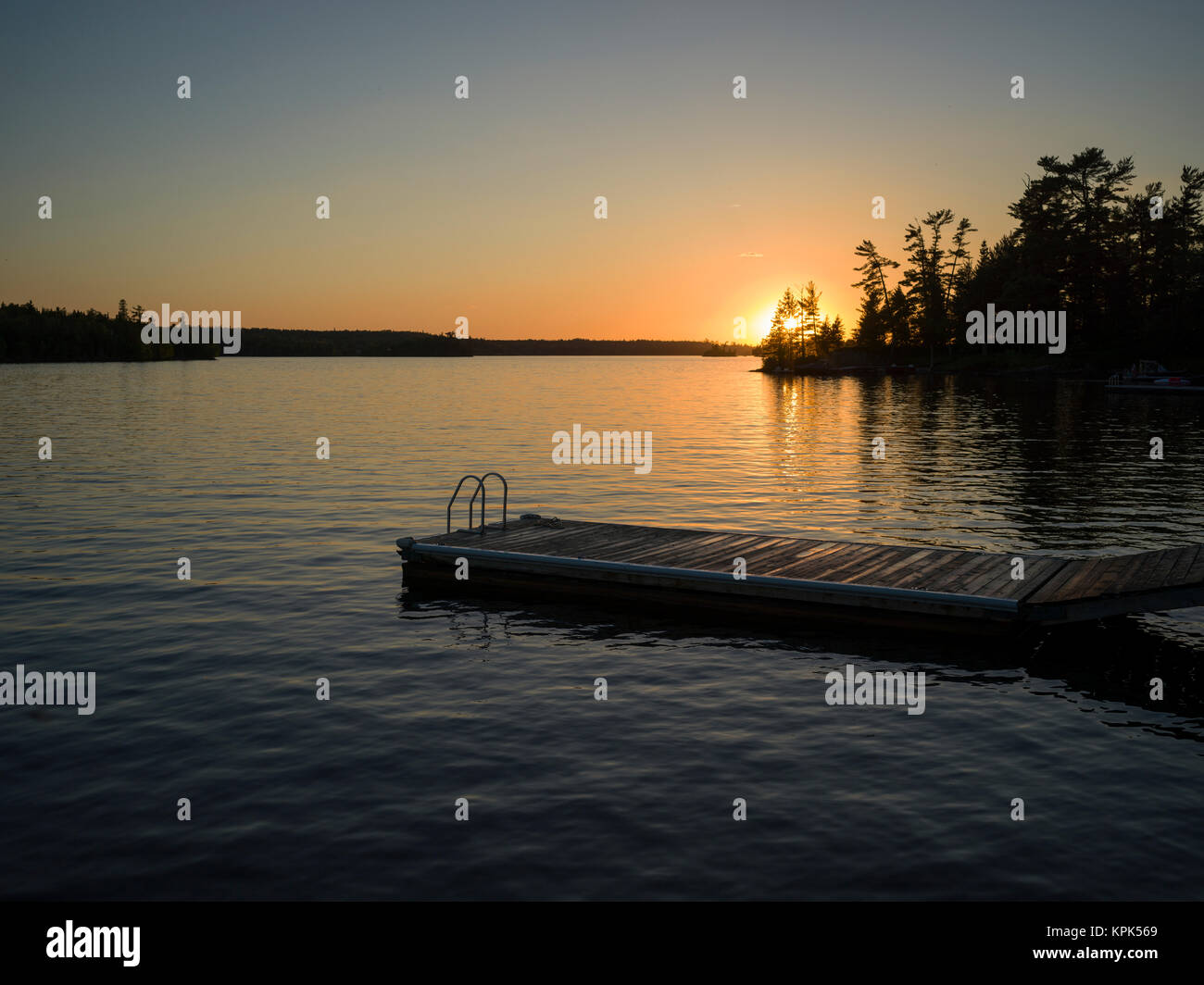 Die Sonne über See des Holzes mit einem Dock im Vordergrund; See des Holzes, Ontario, Kanada Stockfoto