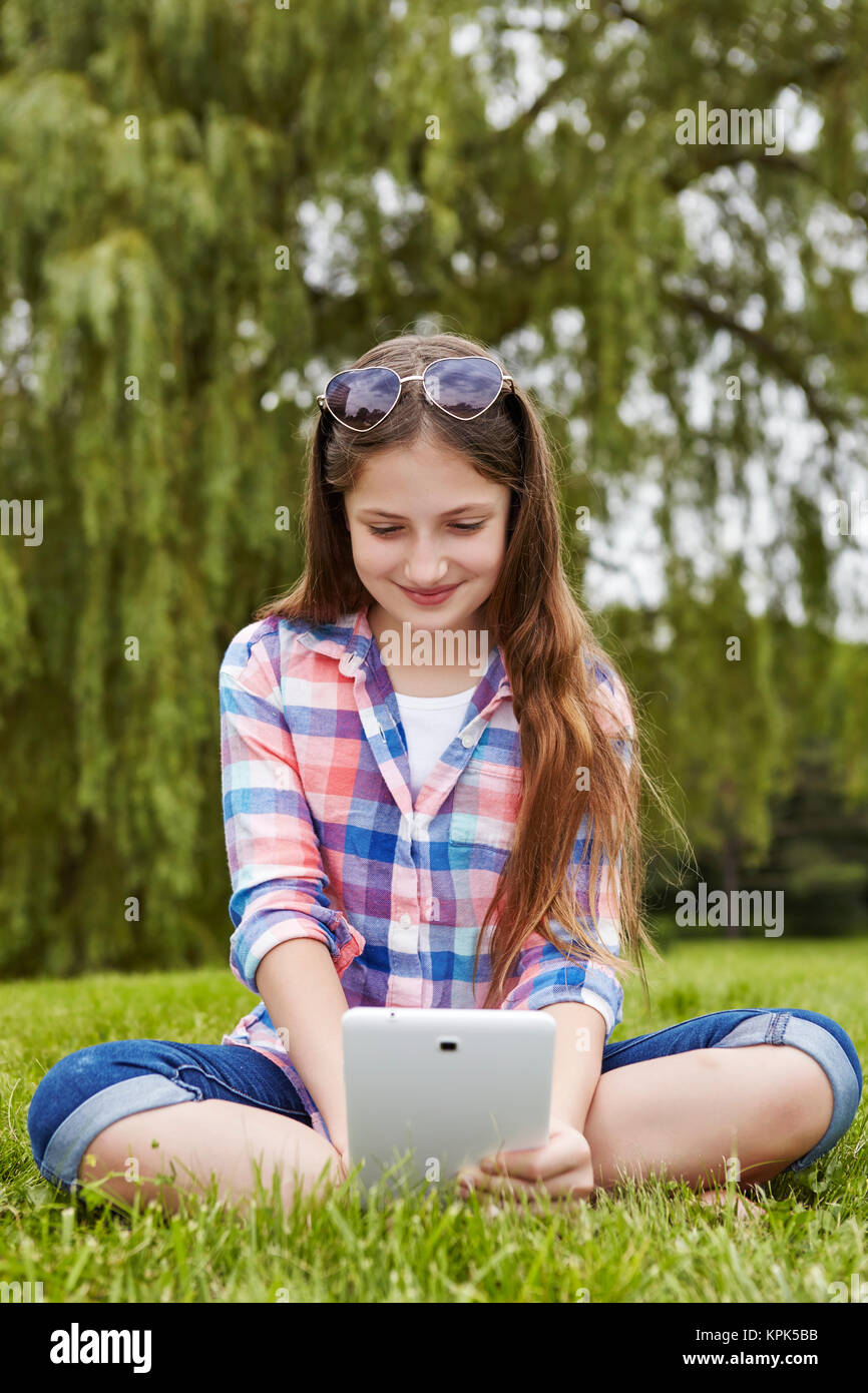 Jugendliche Mädchen in einem Park mit einem Tablet-PC sitzen; Toronto, Ontario, Kanada Stockfoto