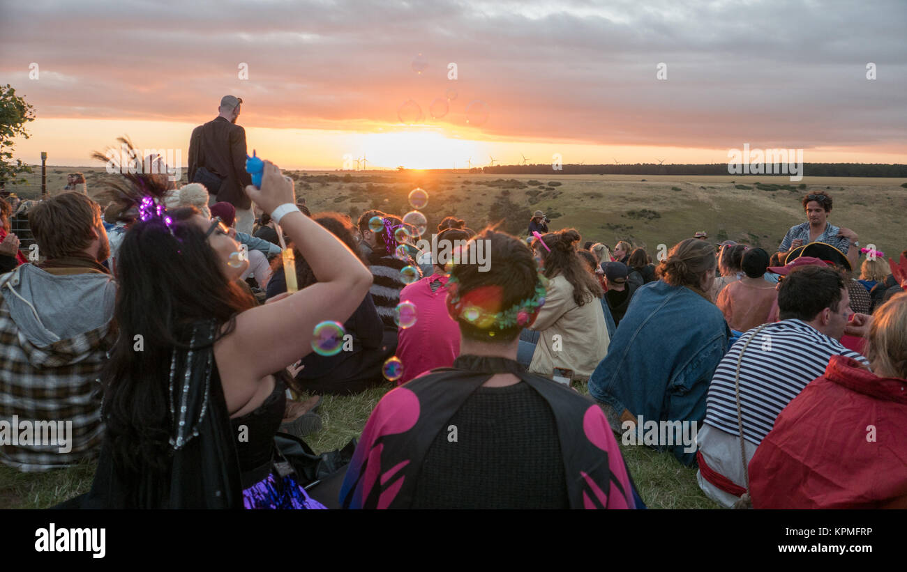 Frauen in der Masse der Musik Festival goers Sitzen, Beobachten Golden Sunset während bläst Seifenblasen. Stockfoto