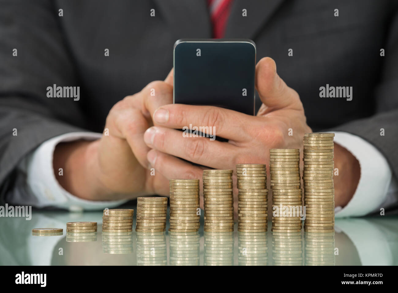 Geschäftsmann mit Smartphone mit gestapelten Münzen Stockfoto