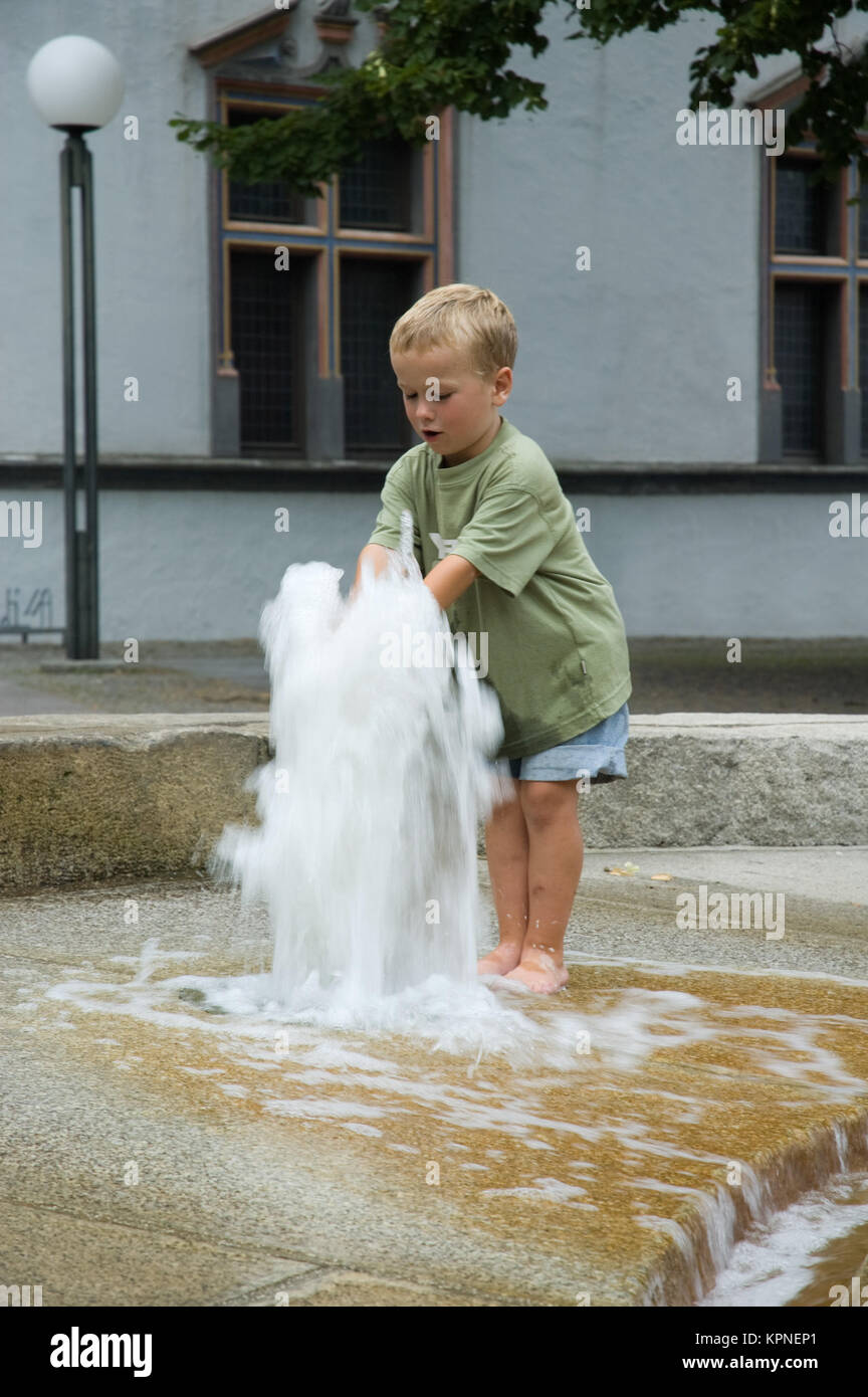 Junge spielt mit Springbrunnen Stockfoto