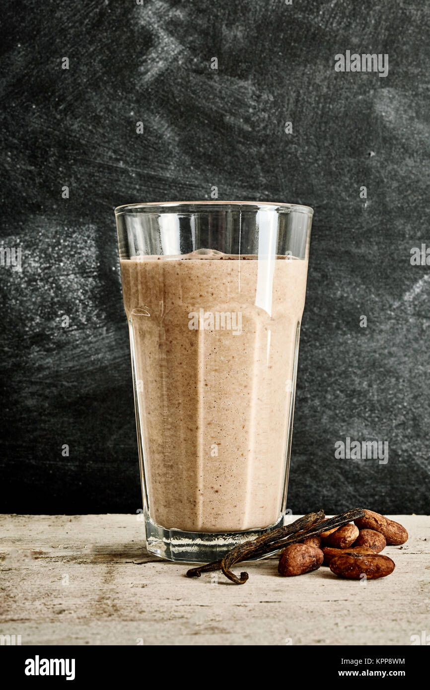 Großes Glas Schokolade Smoothie auf weißem Marmor tisch Neben Vanilla Bean und Kakao Pads gegen einen schwarzen Marmor Hintergrund Stockfoto