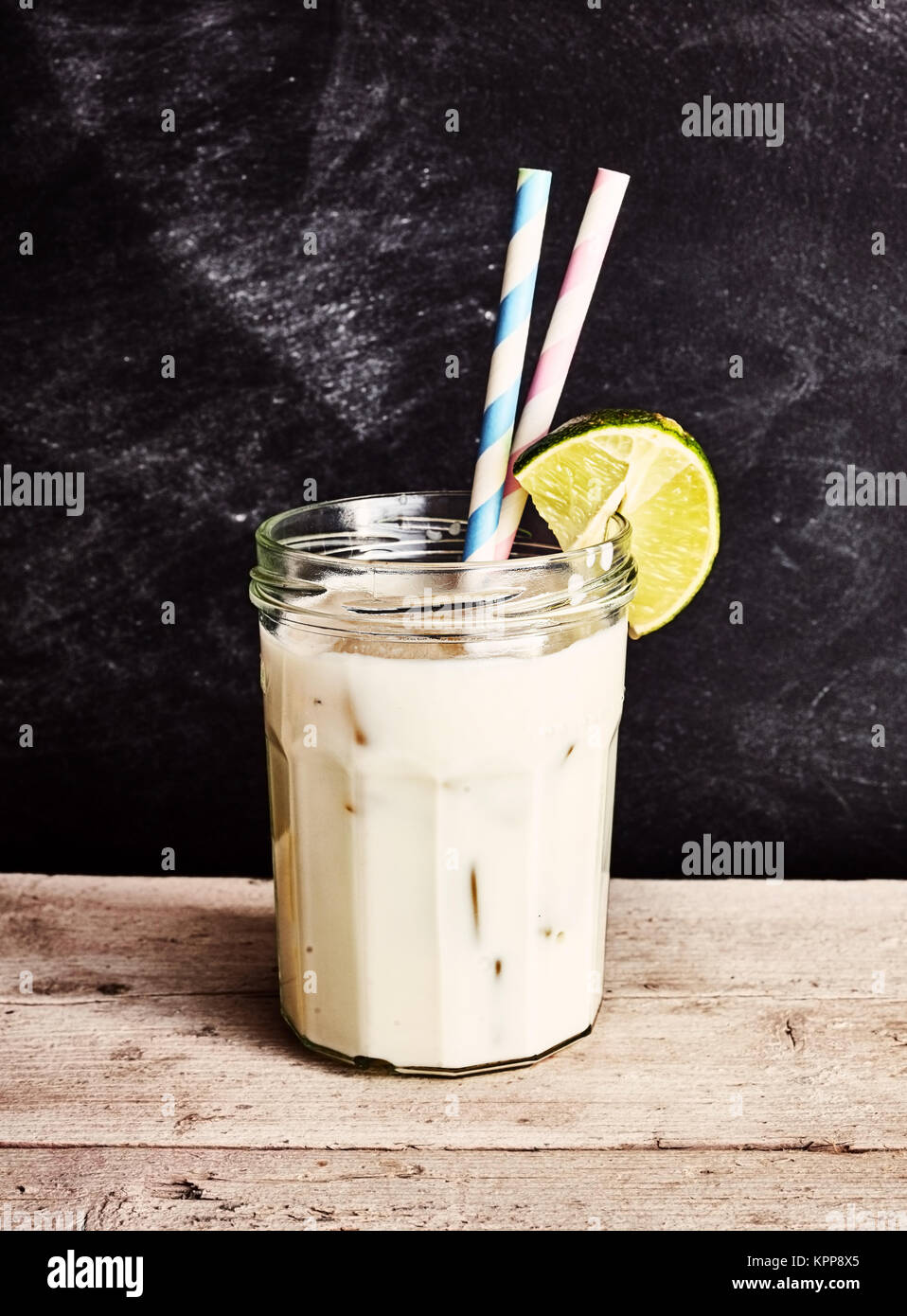 Alkoholische coconut Cocktail in ein Marmeladenglas mit zwei Wirbeln bunte Strohhalme und ein Stück von Kalk auf einen rustikalen Tisch Stockfoto