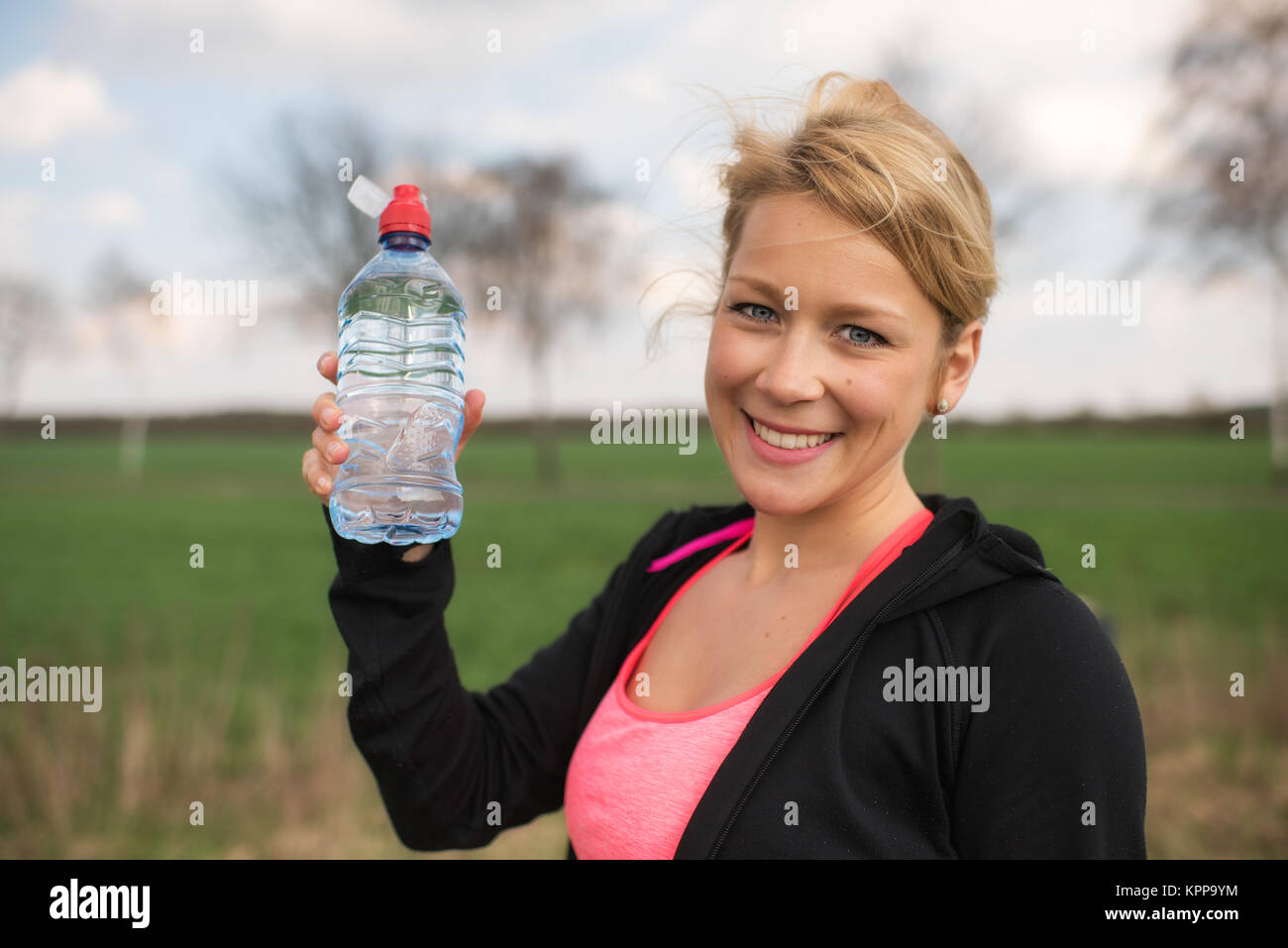 Blonde weibliche Jogger auf einer Wiese mit einer Flasche Wasser Stockfoto