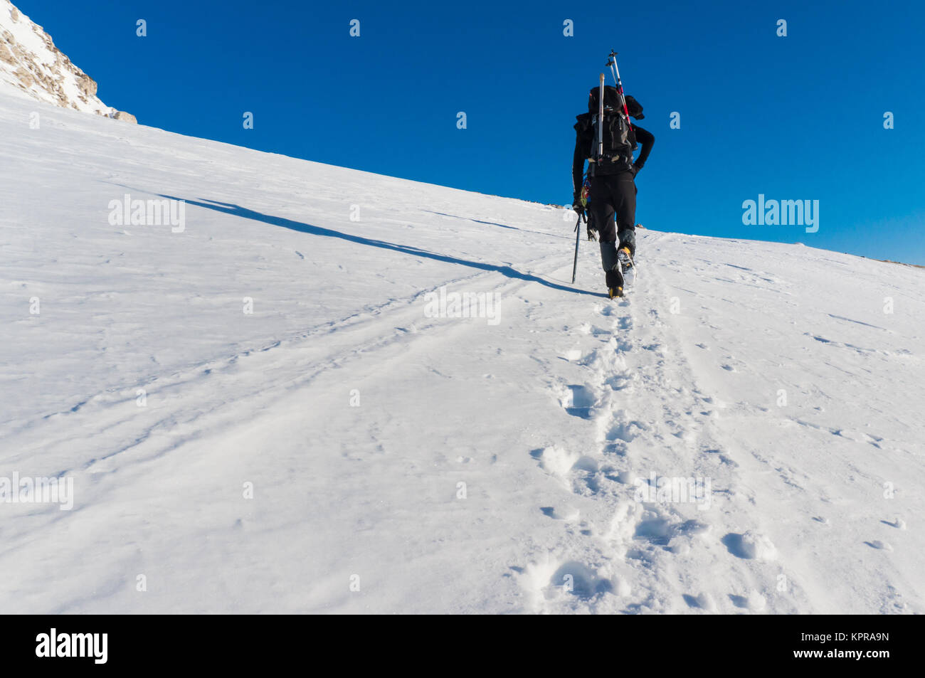 Ein Mann ist, klettern die Berge mit Schnee mit seinen Skiern in seinem Rucksack abgedeckt Stockfoto