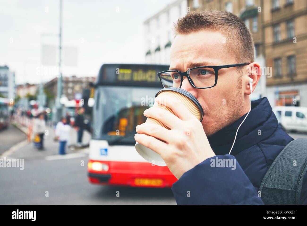 Kaffee am Morgen auf der Straße der Stadt. Junger Mann trinken heißen Kaffee aus der Tasse und Musik im Kopfhörer. Stockfoto