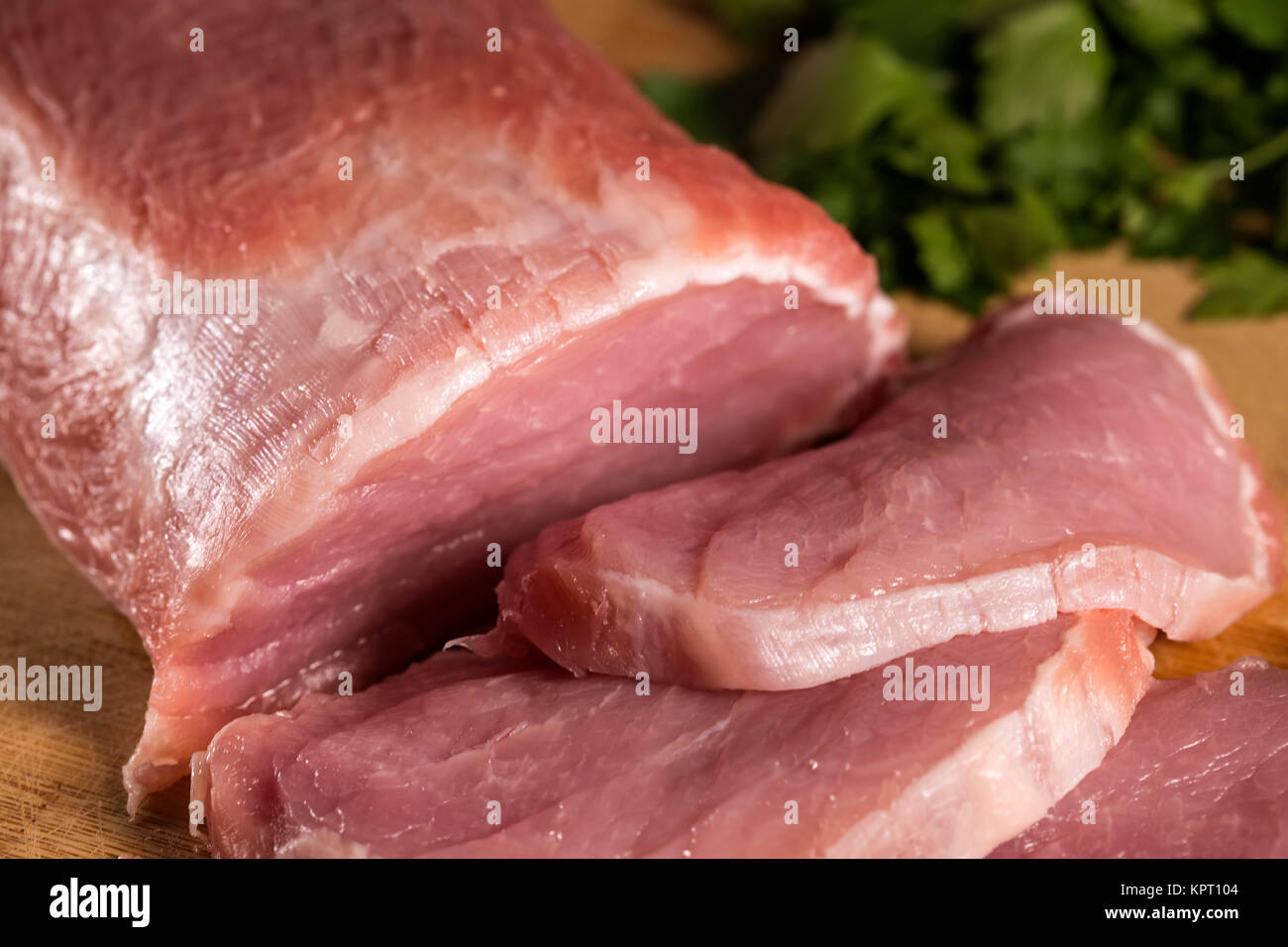 Scheiben von rohem Schweinefleisch auf Holz Schneidbrett chop mit Petersilie im Hintergrund Stockfoto