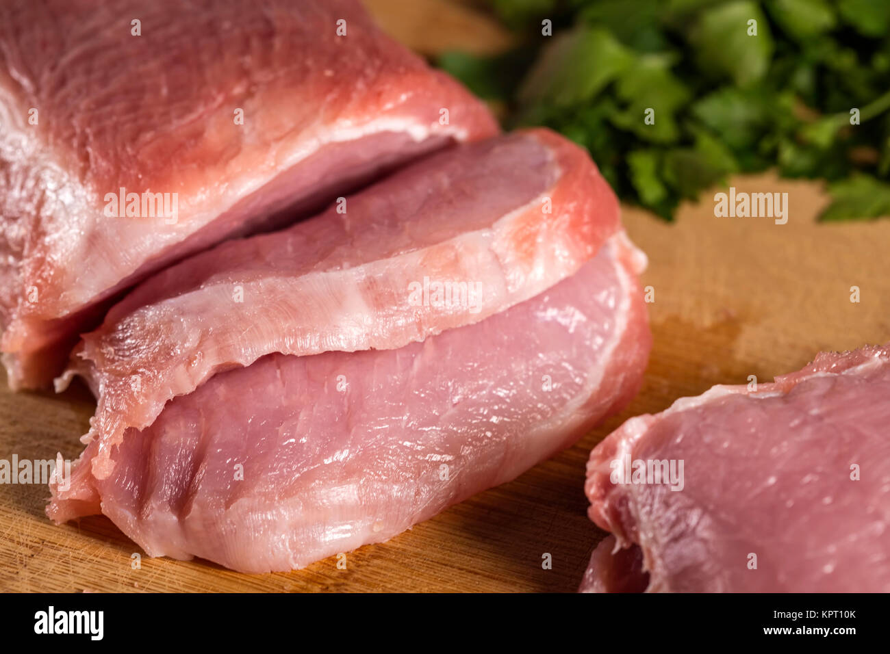 Scheiben von rohem Schweinefleisch auf Holz Schneidbrett chop mit Petersilie im Hintergrund Stockfoto