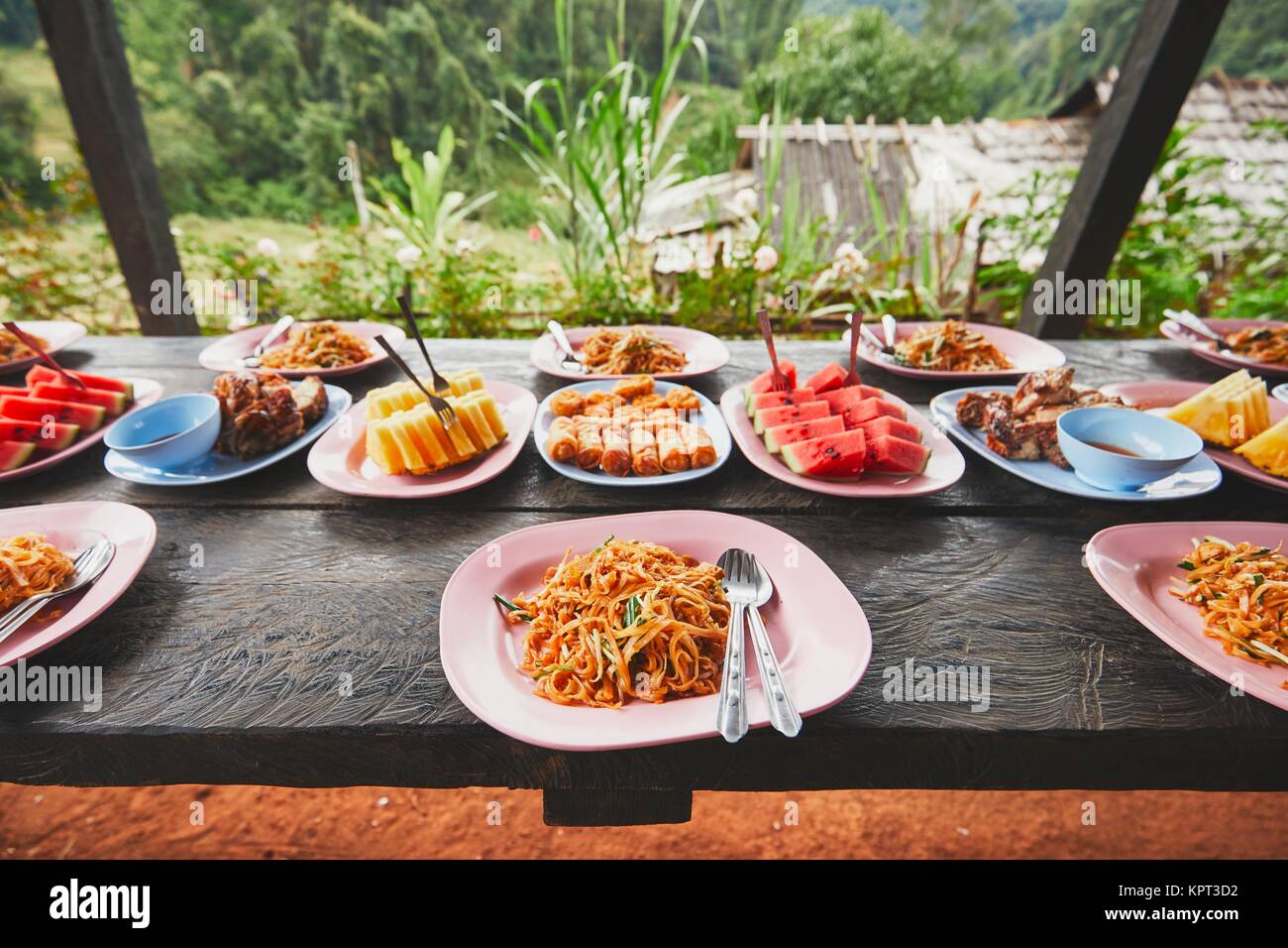 Mittagessen in der Mitte des Dschungels. Der Tisch voller Lebensmittel und Früchte. Traditioal Pad Thai, Frühlingsrollen, Melone und Ananas. Provinz Chiang Mai, Th Stockfoto