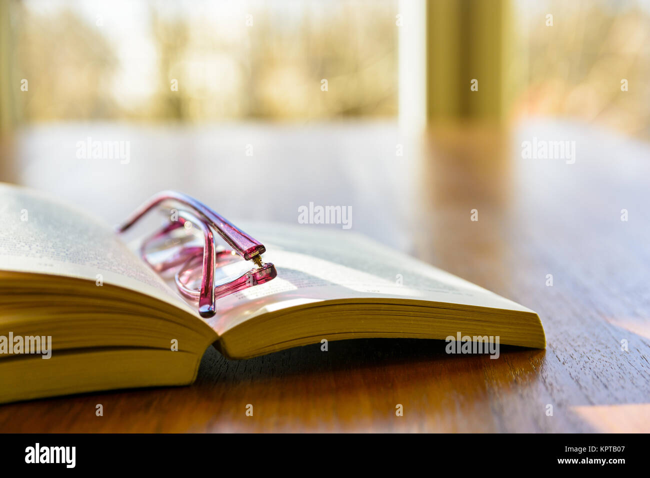 Nahaufnahme einer offenen Tasche Buch mit einer Lesebrille, flach auf einem  Tisch vor dem Fenster Stockfotografie - Alamy