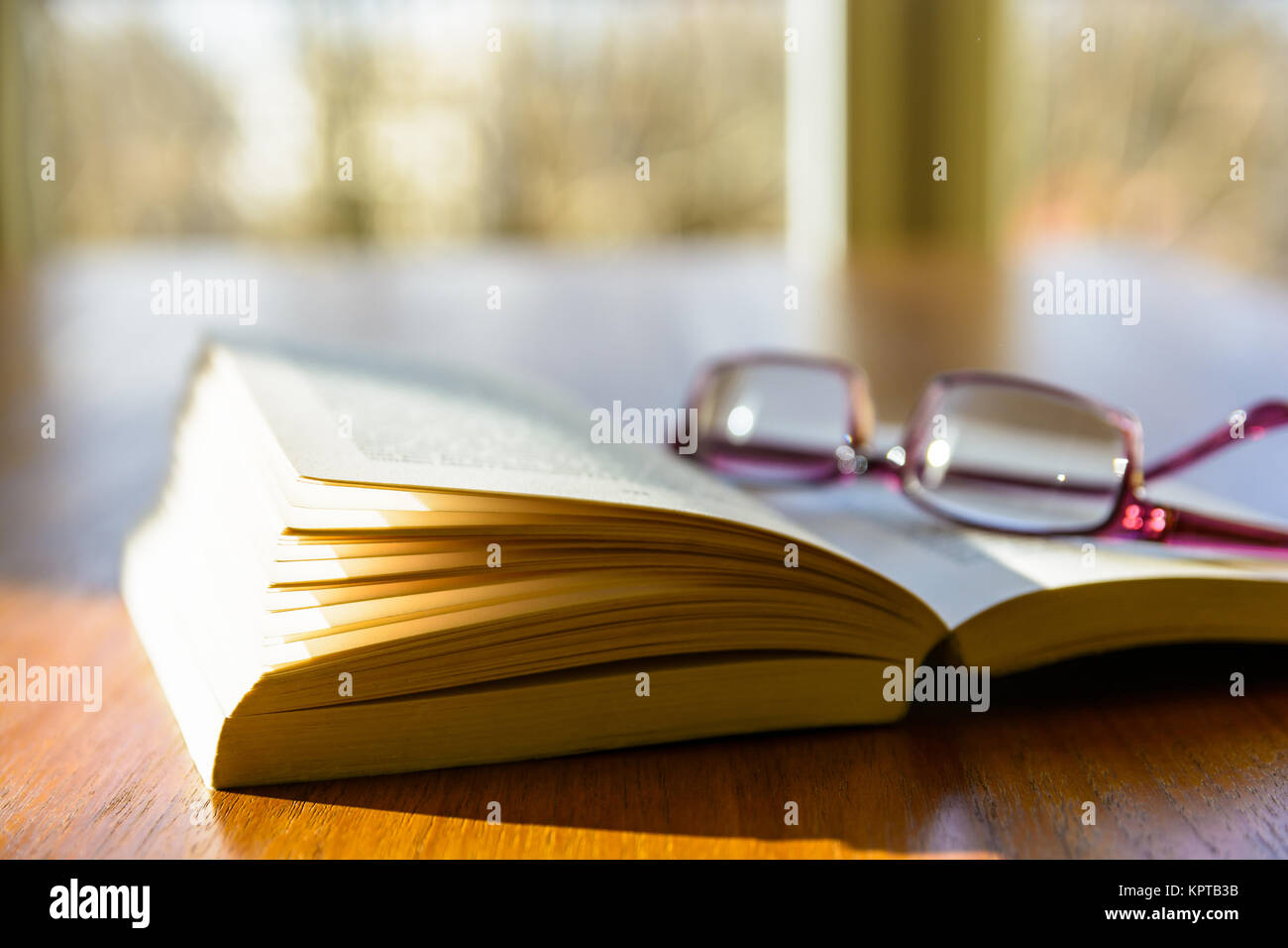 Nahaufnahme einer offenen Tasche Buch mit einer Lesebrille, flach auf einem Holztisch und von einem Strahl der Sonne beleuchtet, in Fron Stockfoto