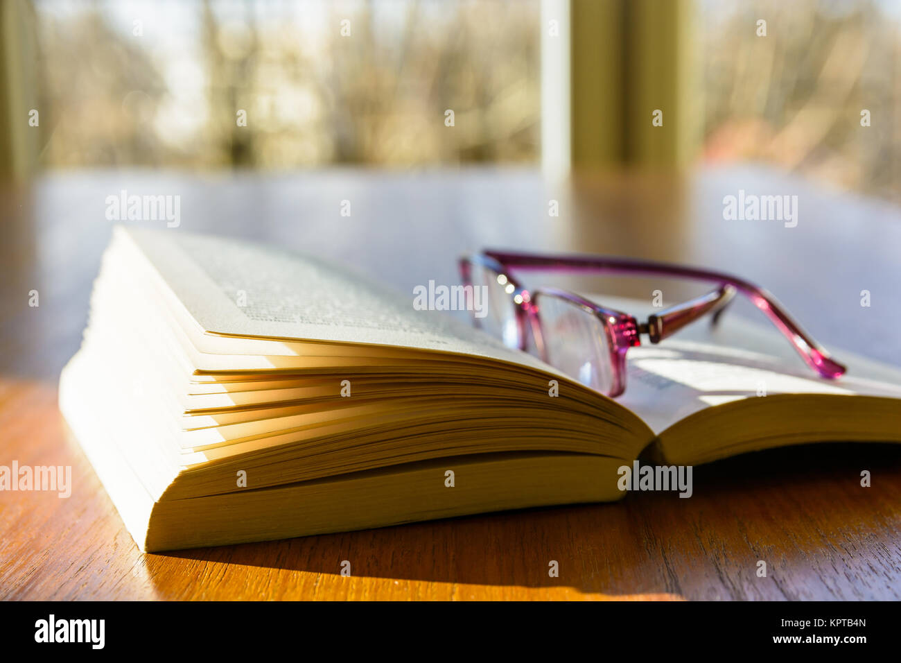 Nahaufnahme einer offenen Tasche Buch mit einer Lesebrille, flach auf einem Holztisch und von einem Strahl der Sonne beleuchtet, in Fron Stockfoto
