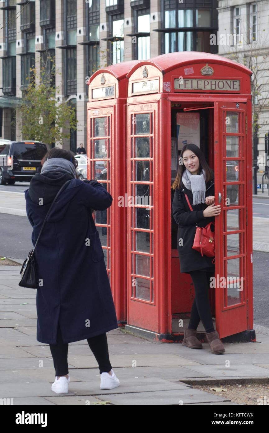 Asiatische Touristen fotografieren in einem traditionellen britischen Telefonzelle Stockfoto