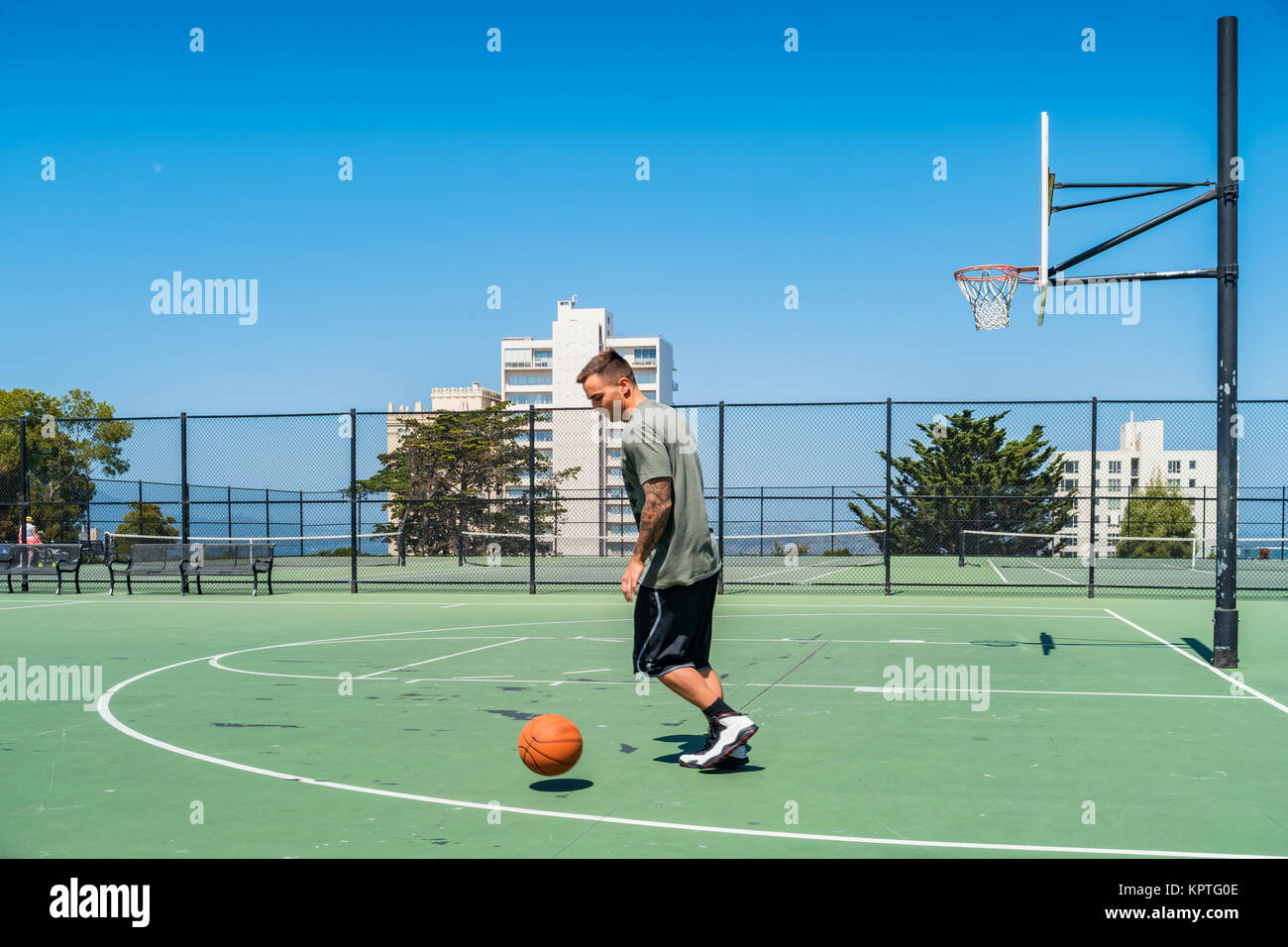 Junger Mann spielt Basketball an der öffentlichen Alice Marmor Tennisplätze in San Francisco, Kalifornien. Stockfoto