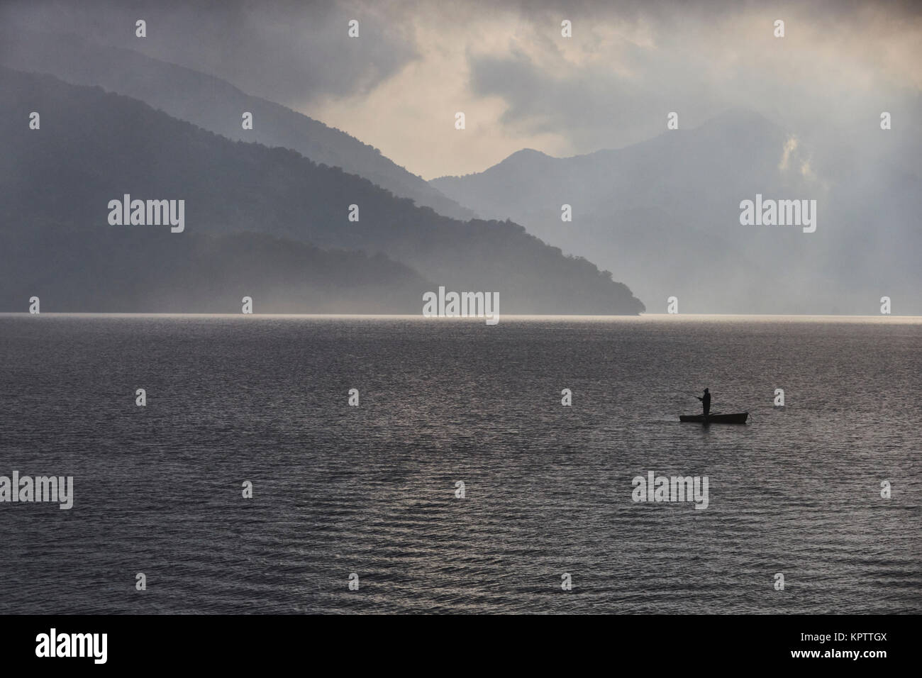 Einsame Fischer in einem Boot auf dem See Chuzenji während bewölkter Sonnenuntergang vor dem Regen. 一人で中禅寺湖に釣り。 Stockfoto