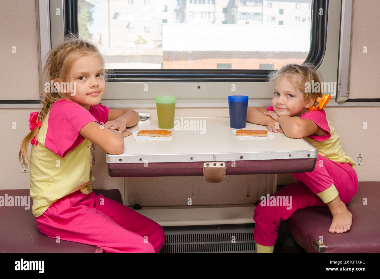 Zwei kleine Mädchen im Zug sitzen am Tisch in der Außenborder zweiter Klasse Wagen in der gleichen Kleidung Stockfoto