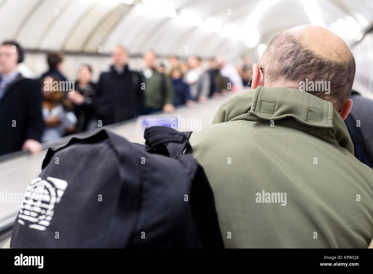 Mann mit Glatze und Menschen defokussierten und unscharf im Hintergrund Fahrt mit der Londoner U-Bahn Fahrtreppen in England Stockfoto