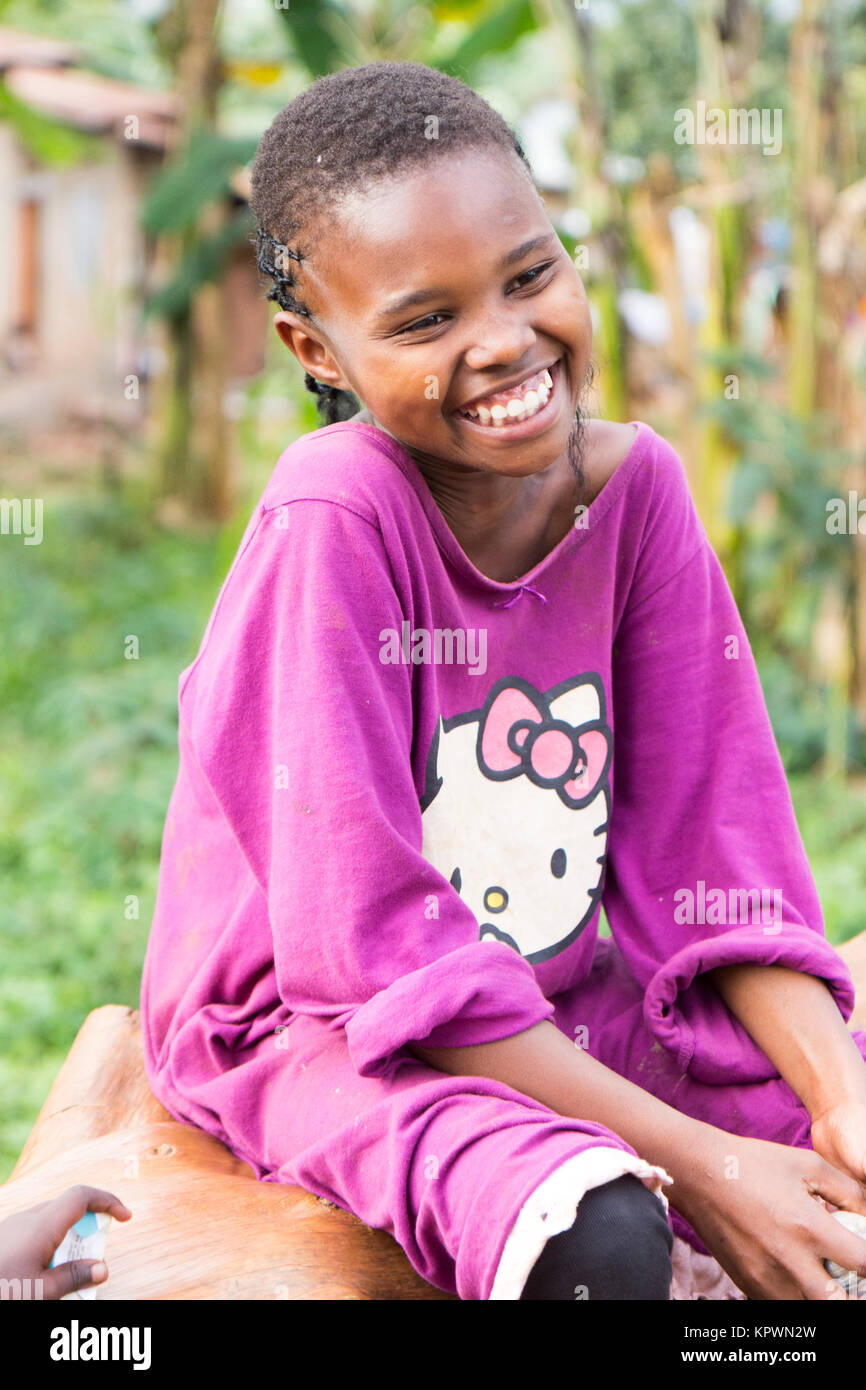 Ein schönes Lachen ugandischen Mädchen sitzen auf einen umgestürzten Baumstamm. Stockfoto