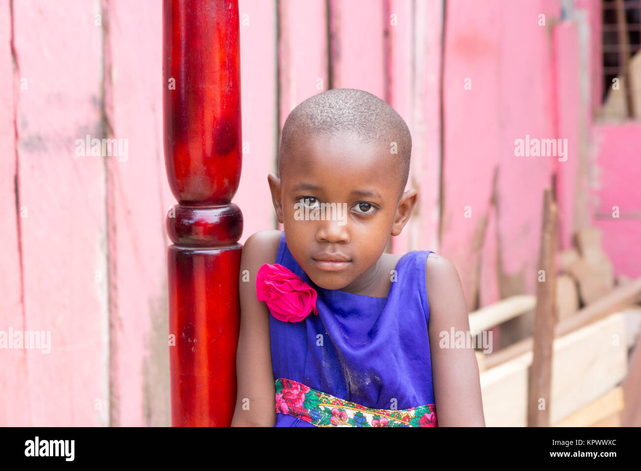 Eine schöne Ugandischen lächelnde Mädchen. Sie ist in einem blauen Kleid mit einem rosa Blume darauf gekleidet. Stockfoto