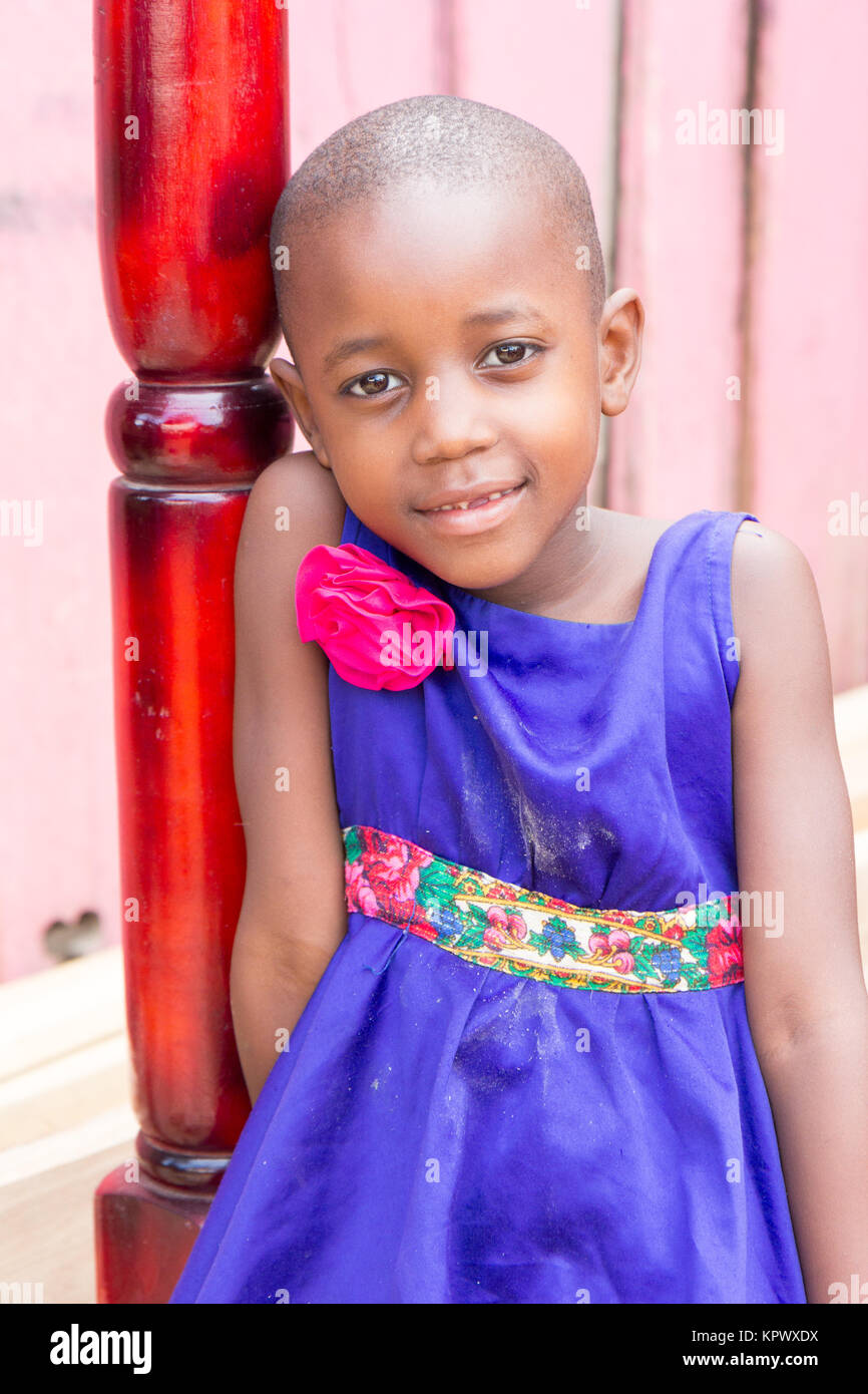 Eine schöne Ugandischen lächelnde Mädchen. Sie ist in einem blauen Kleid mit einem rosa Blume darauf gekleidet. Stockfoto