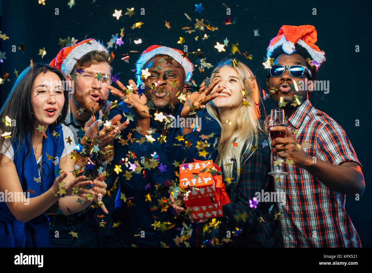 Freunde bei Party des neuen Jahres, das tragen Nikolausmützen, Tanzen und Blasen Konfetti Stockfoto