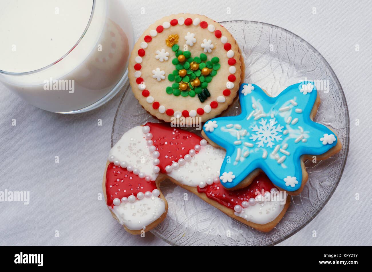 Drei Weihnachten schneiden Sie Cookies auf einer Glasplatte mit einem Glas Milch Stockfoto