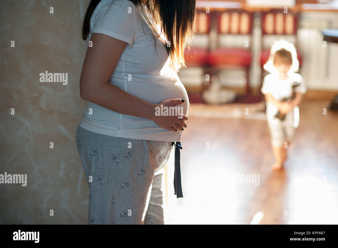 Schwangere Frau, die auf dem Hintergrund spielt die älteste Tochter. Zuhause Stockfoto