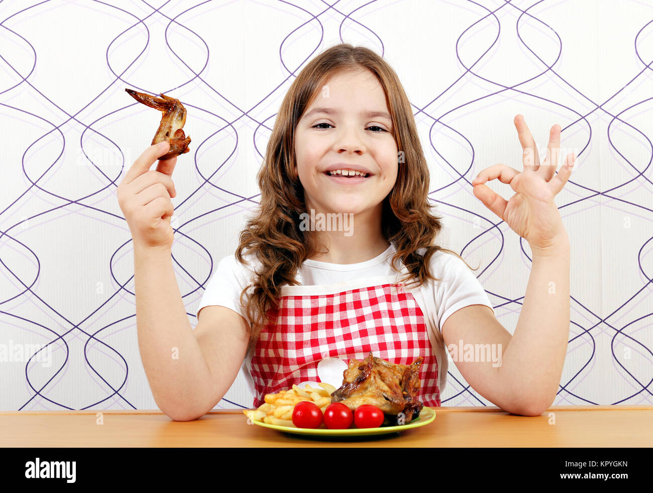 Glückliche kleine Mädchen mit gerösteten Chicken Wings und ok Handzeichen Stockfoto