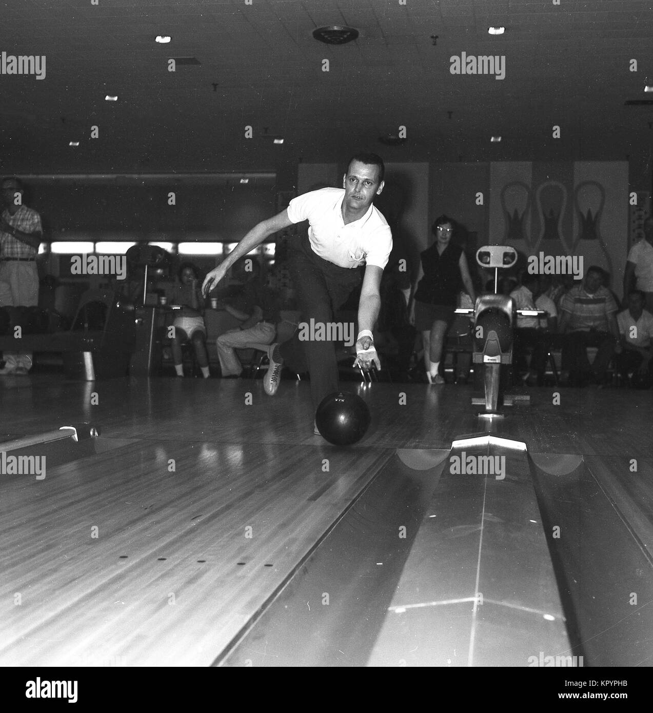 1960, historische, Ten-pin Bowling, eine beliebte Freizeitaktivität dieser Zeit, ein Mann mit einem Kurzarm Shirt und ein Bowling Glove wirft eine Bowling Kugel unten eine Lane, mit Menschen, die hinter der Suche auf, USA. Stockfoto
