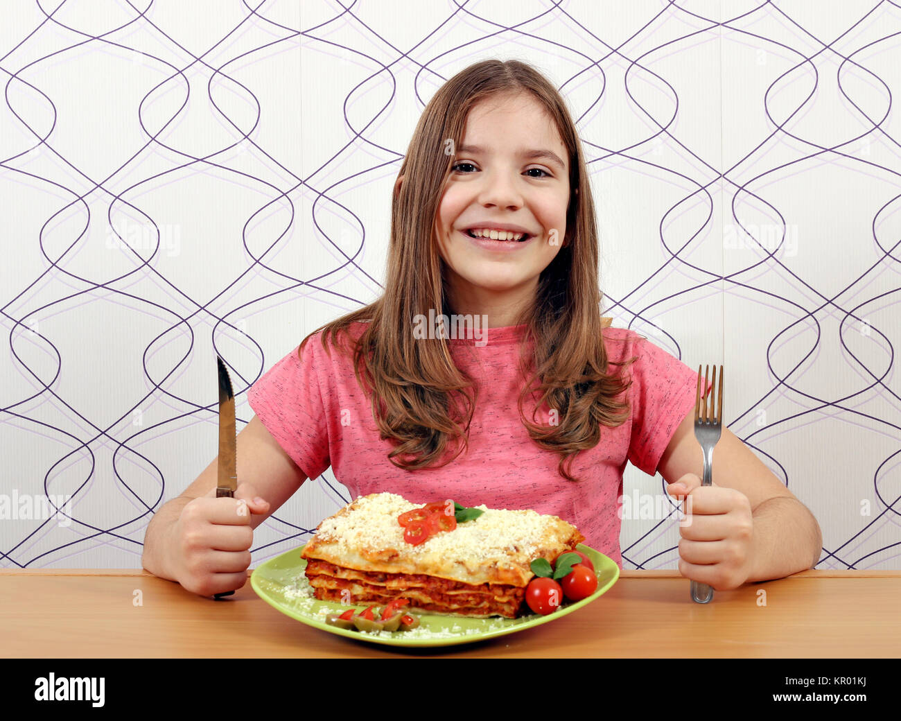 Glückliche kleine Mädchen mit Lasagne auf Tisch Stockfoto