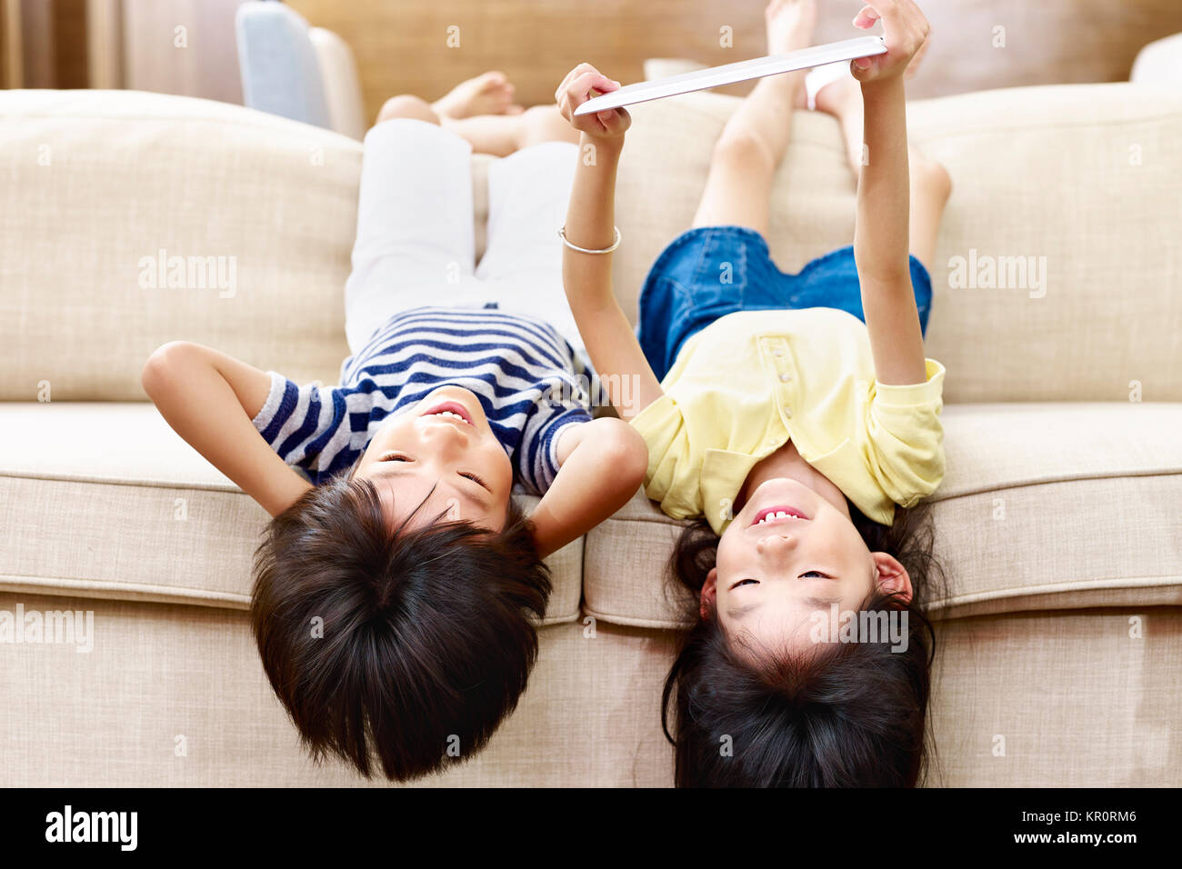 Zwei asiatische Kinder Jungen und Mädchen liegen auf den Kopf auf der Couch bei digital Tablet. Stockfoto