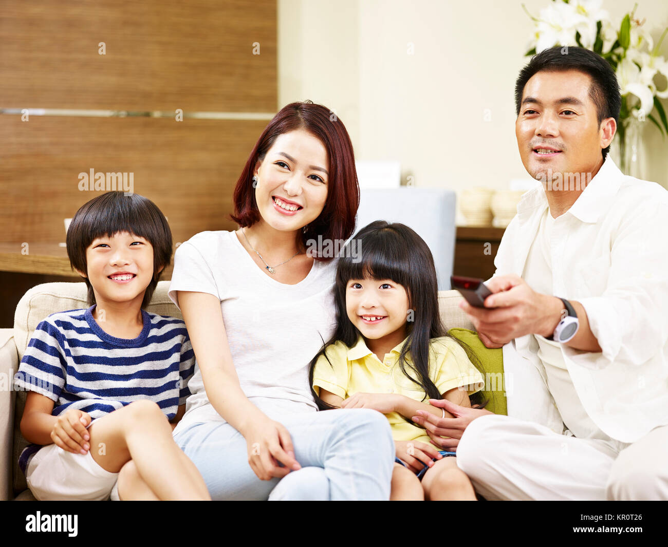 Gerne asiatische Familie mit zwei Kindern sitzt auf der Couch zu Hause vor dem Fernseher. Stockfoto