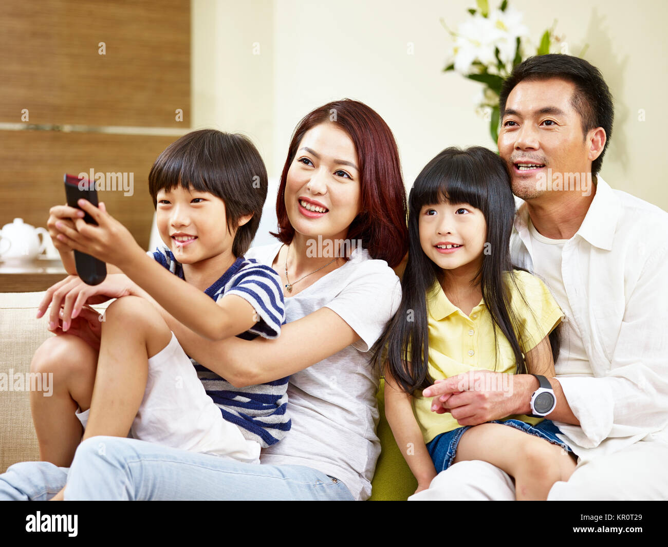 Gerne asiatische Familie mit zwei Kindern sitzt auf der Couch zu Hause vor dem Fernseher. Stockfoto