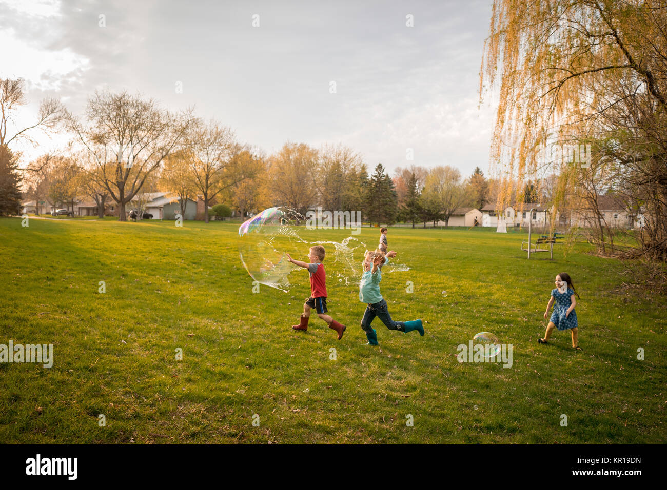 Vier Kinder jagen riesige Seifenblasen in einem öffentlichen Park Stockfoto