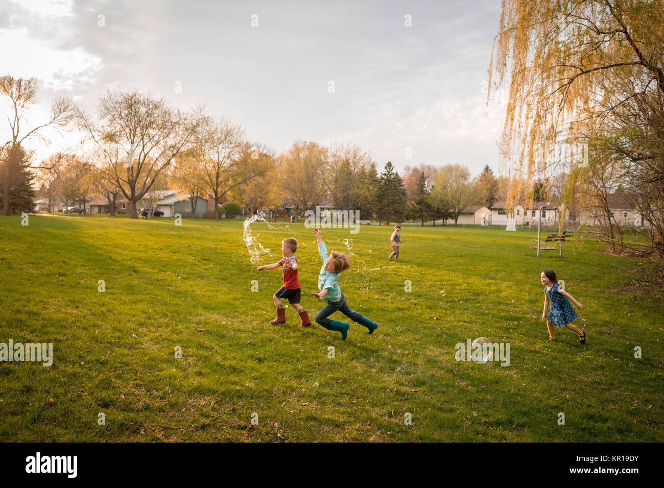 Vier Kinder jagen riesige Seifenblasen in einem öffentlichen Park Stockfoto