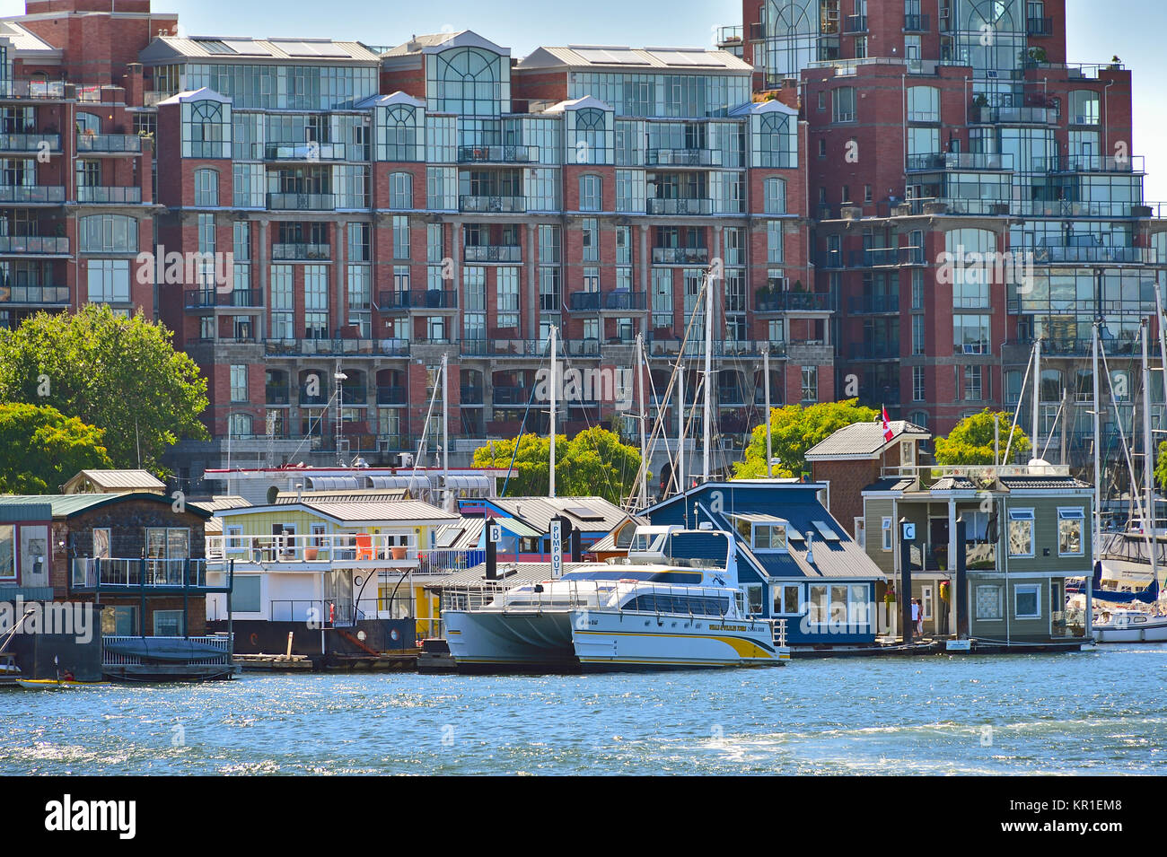 Eine Gruppe von schwimmenden Häusern Lin bis zu einem Dock vor einem großen Gebäudekomplex am Hafen Victoria auf Vancouver Island, British Columbia, Kanada. Stockfoto