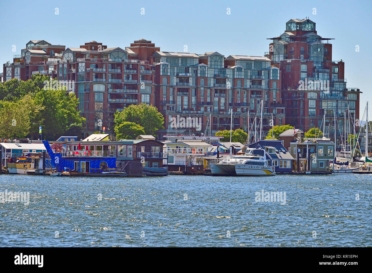 Eine Gruppe von schwimmenden Häusern Lin bis zu einem Dock vor einem großen Gebäudekomplex am Hafen Victoria auf Vancouver Island, British Columbia, Kanada. Stockfoto