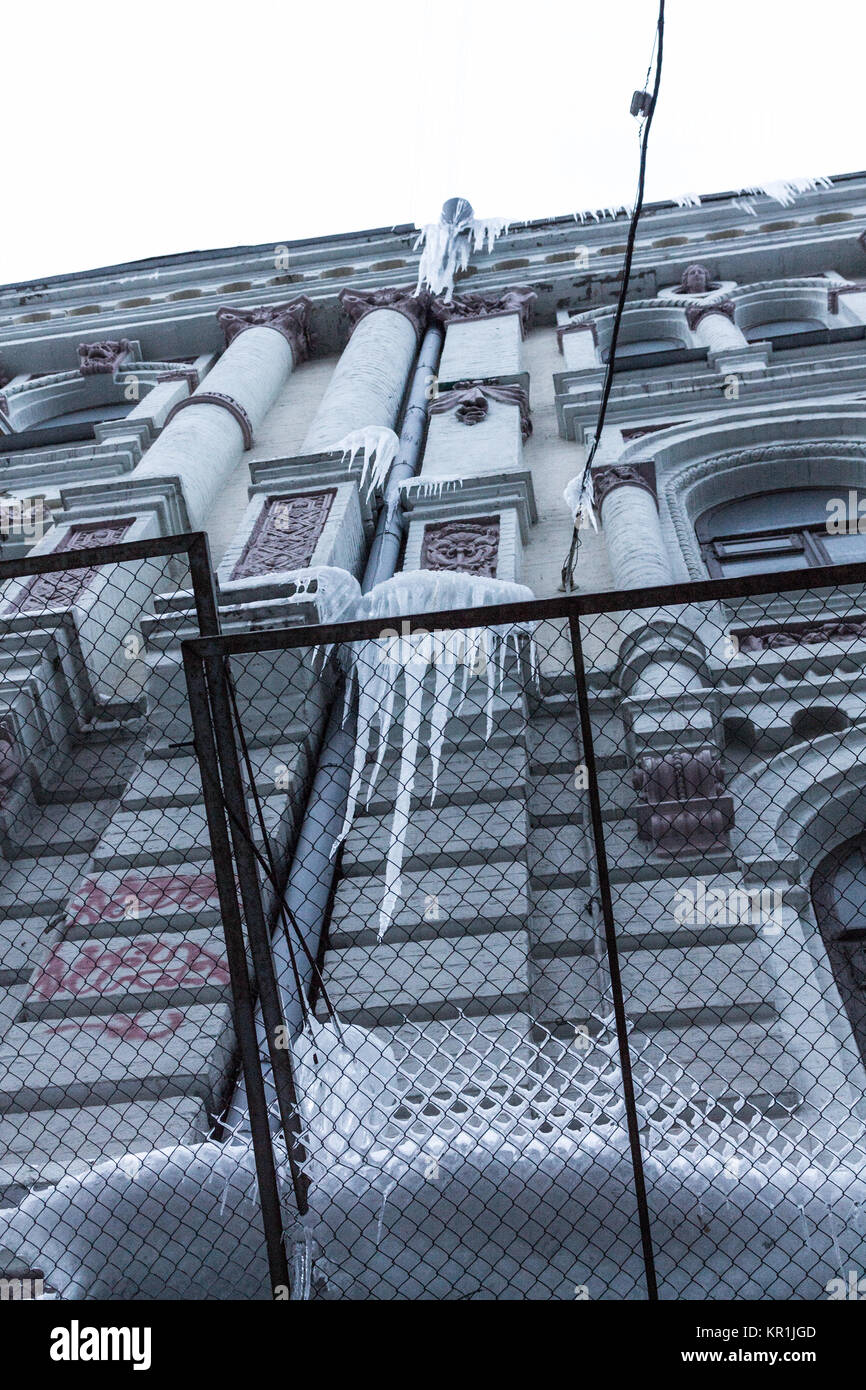 Ein mehrstöckiges Haus mit Ice Eiszapfen. Eiszapfen hingen über der Fahrbahn der Stadt. Gefährliche hängenden Eiszapfen. Stockfoto