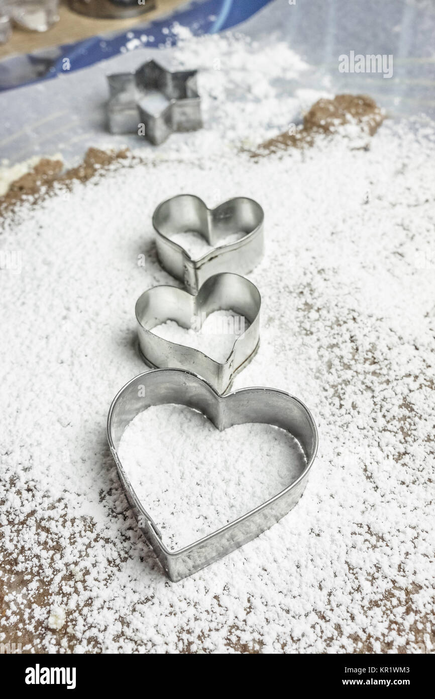 Drei herzförmige Plätzchenausstecher auf eine Paste in Puderzucker bedeckt. Diese Messer sind traditionelle Weihnachtsplätzchen zu machen. Backen Liebe Konzept. Stockfoto