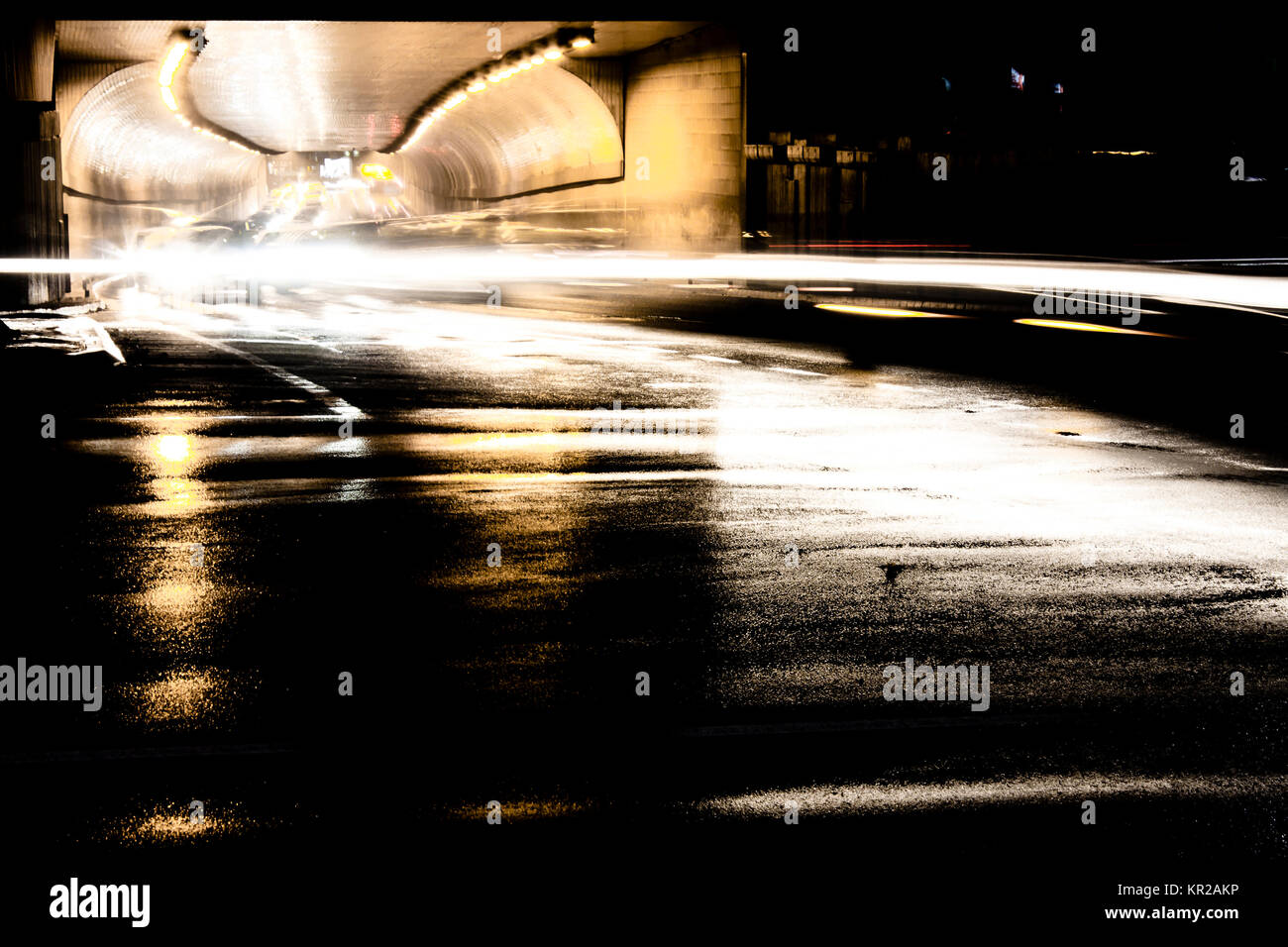 Blurry Nacht Verkehr im Tunnel und auf regennassen Straßen Kreuzung mit leichten Wanderwegen und Reflexionen auf nassem Asphalt. Stockfoto