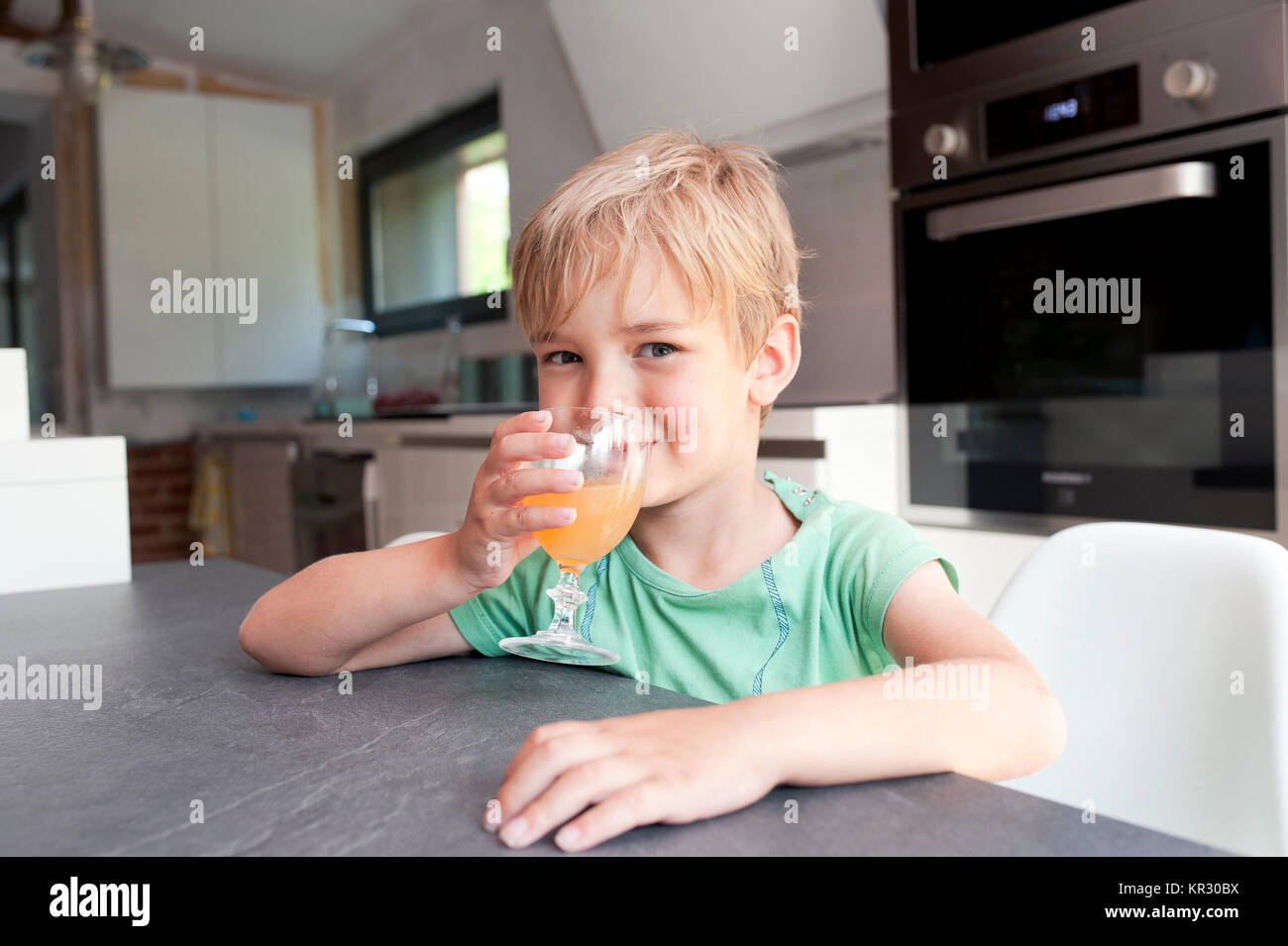 Kind in einer Küche trinkt ein Glas Fruchtsaft Stockfoto