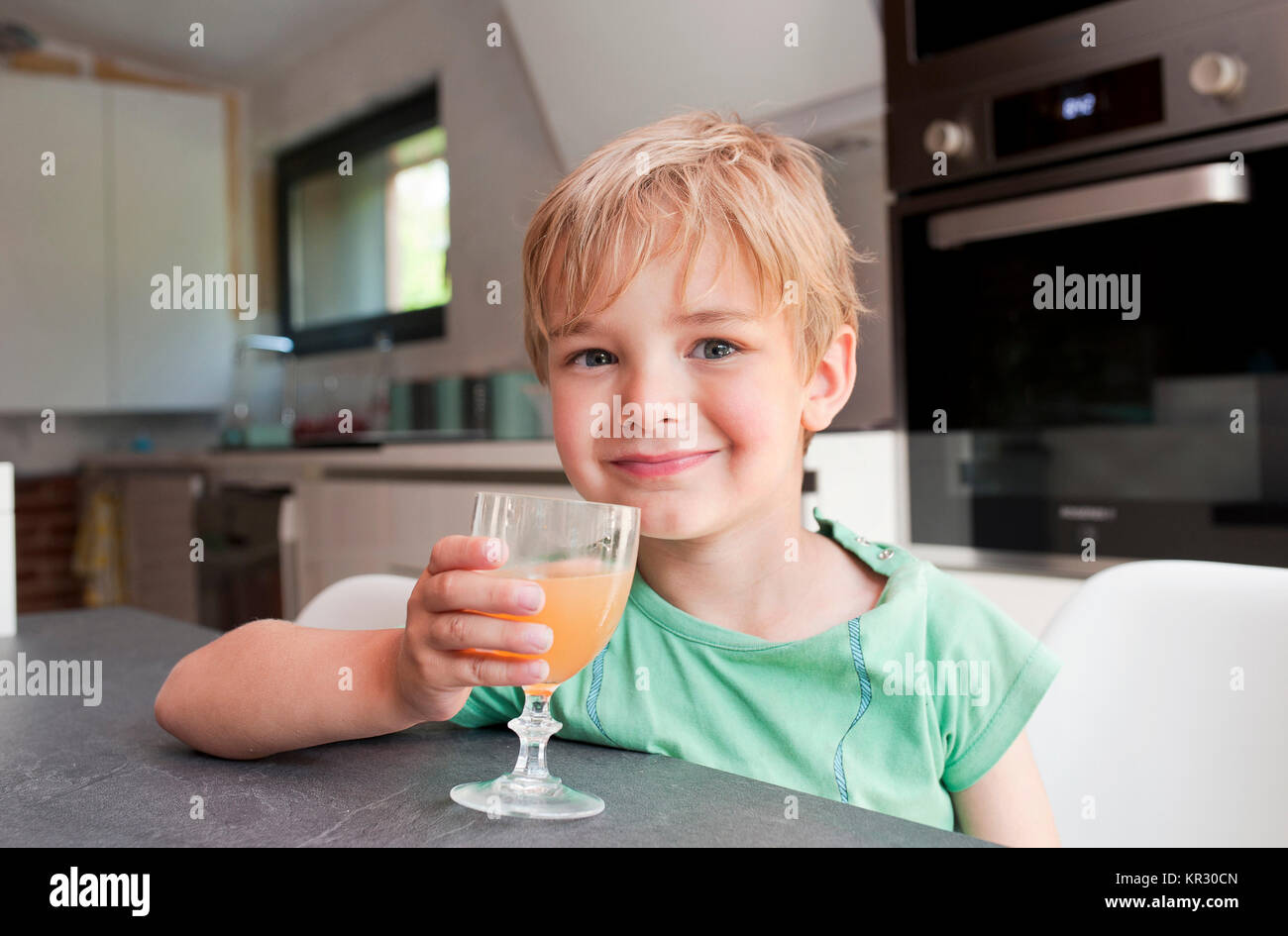 Kind in einer Küche trinkt ein Glas Fruchtsaft Stockfoto