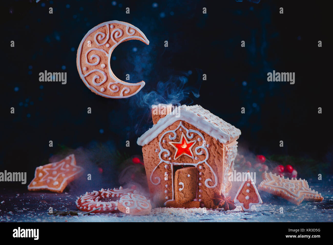 Weihnachten backen Konzept mit einem Lebkuchenhaus, glänzenden Karamell Windows, Keks Mondsichel und steigenden Rauch aus einem Schornstein festlichen Essen Hg Stockfoto