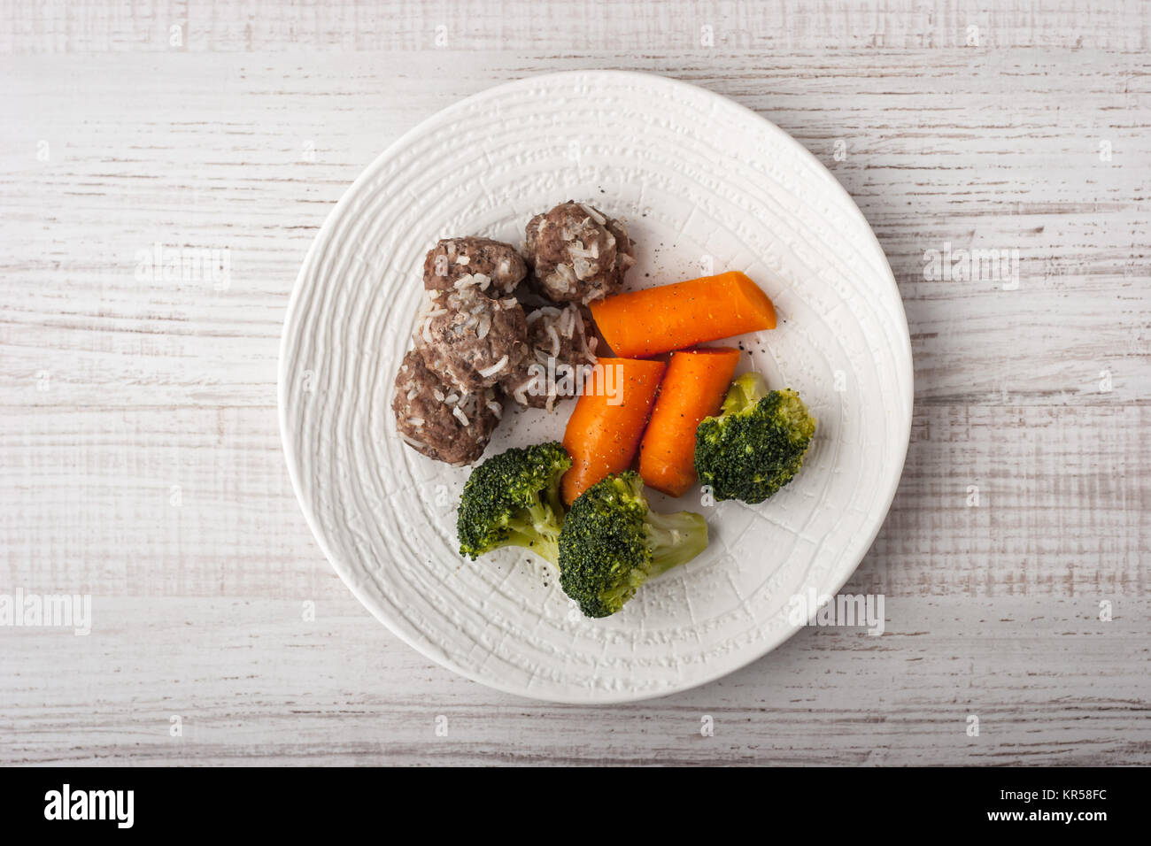 Gedämpfte Broccoli und Karotten mit Frikadellen auf dem weißen Teller Draufsicht Stockfoto