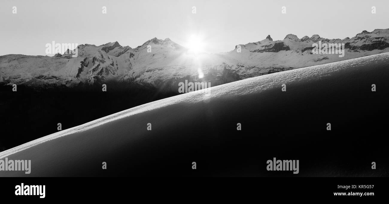 Schöne schwarzweiß Sonnenaufgang in der verschneiten Berglandschaft. Sonnenstrahlen erhellt unberührten Pulverschnee. Alpen, Schweiz. Stockfoto