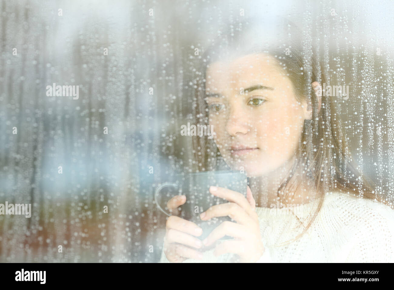 Porträt einer Sehnsucht jugendlich durch ein Fenster allein zu Hause in einer regnerischen Tag suchen Stockfoto