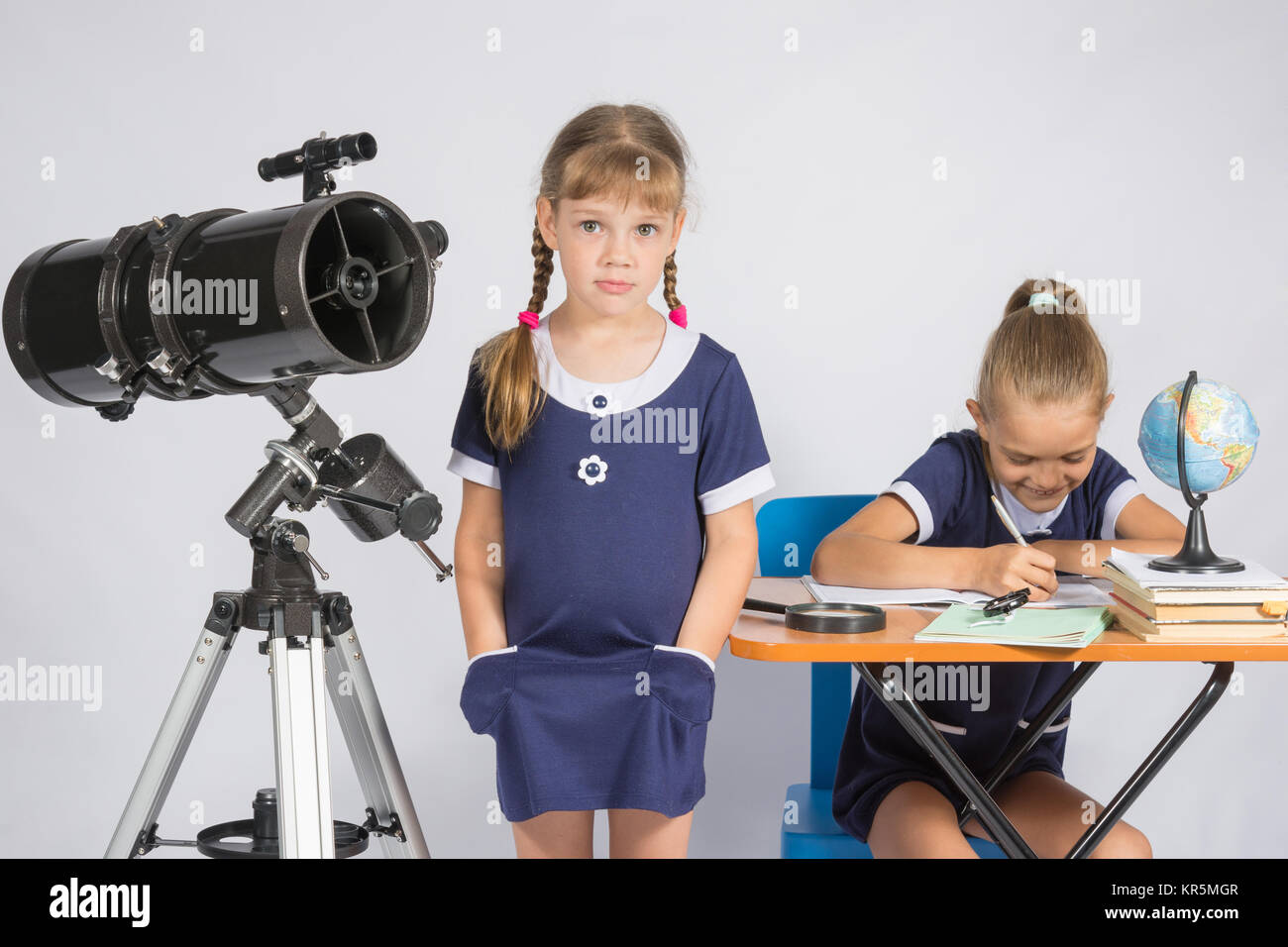 Eine Mädchen steht ein Teleskop mit seinen Händen in den Hosentaschen, ein anderes Mädchen Spaß sitzen am Tisch und schreibt Stockfoto