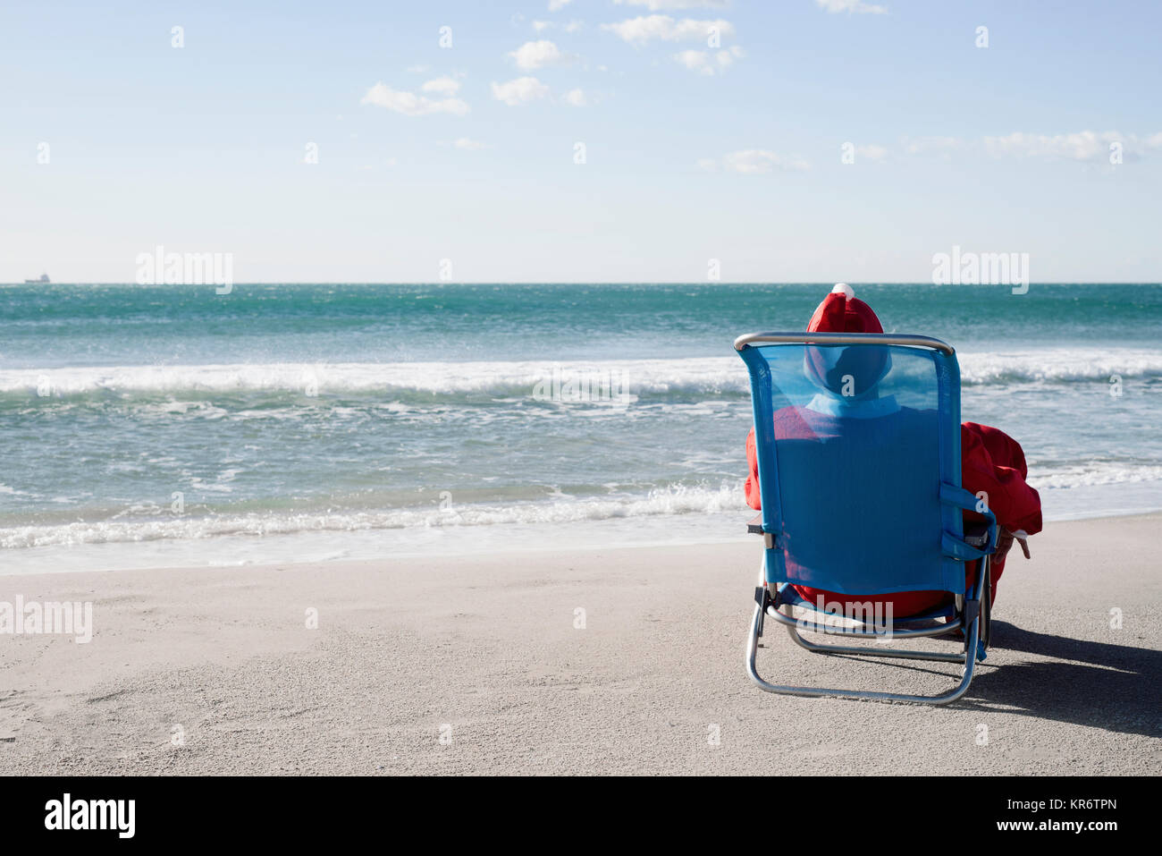 Santa Claus, von hinten gesehen, sitzen in einem Liegestuhl am Strand mit Blick auf den Horizont Stockfoto