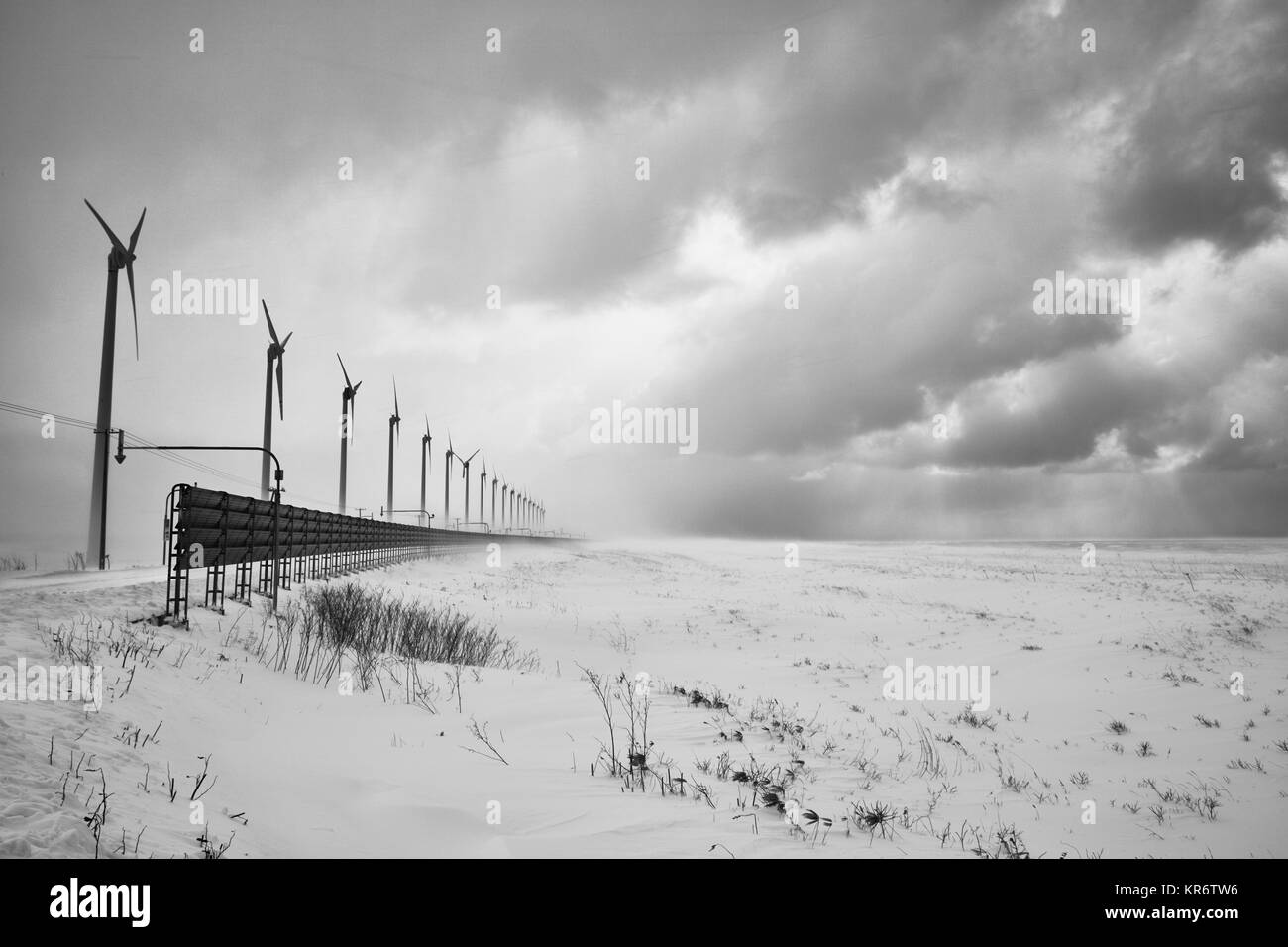 Verschneite Winterlandschaft unter einem bewölkten Himmel, mit einer Reihe von Windenergieanlagen. Stockfoto